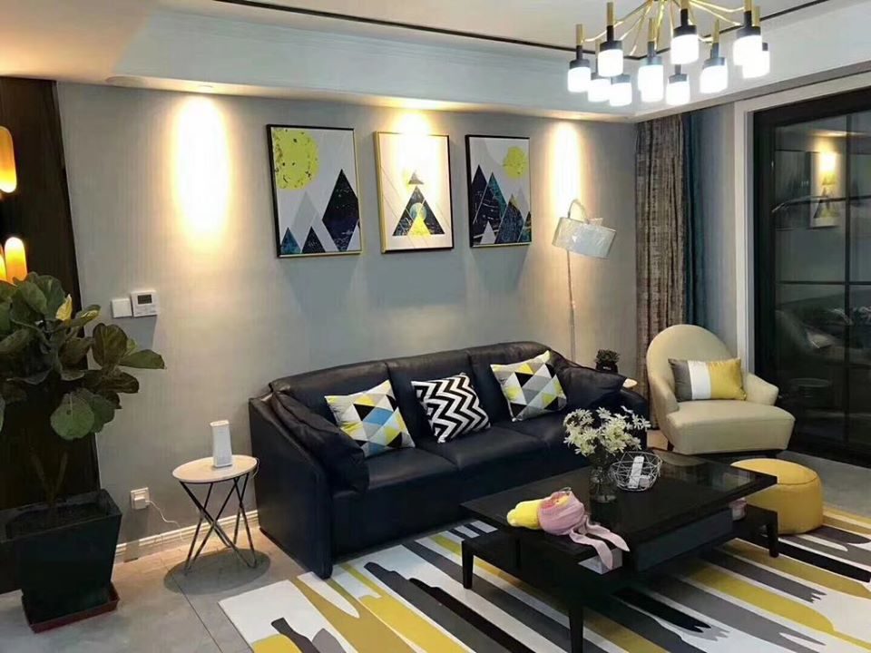 Small Contemporary Living Room designed with Black Coloured Leather upholstered Sofa, Off-white Coloured Sofa Chair, Glass Top Rectangular Wooden Coffee Table placed on a Rug