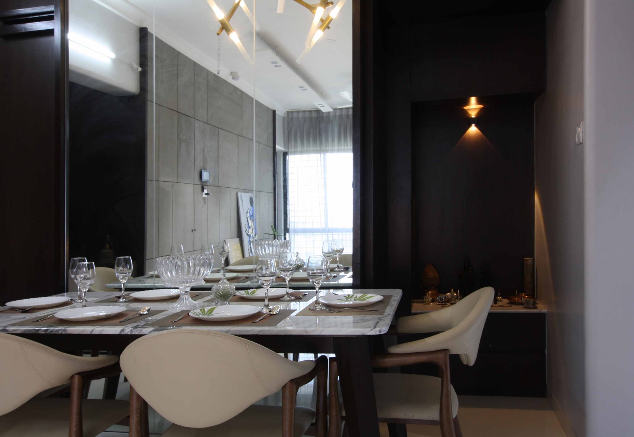 A dark frame marble topped dining table with elegant glassware and dining chairs having crème colour covering.