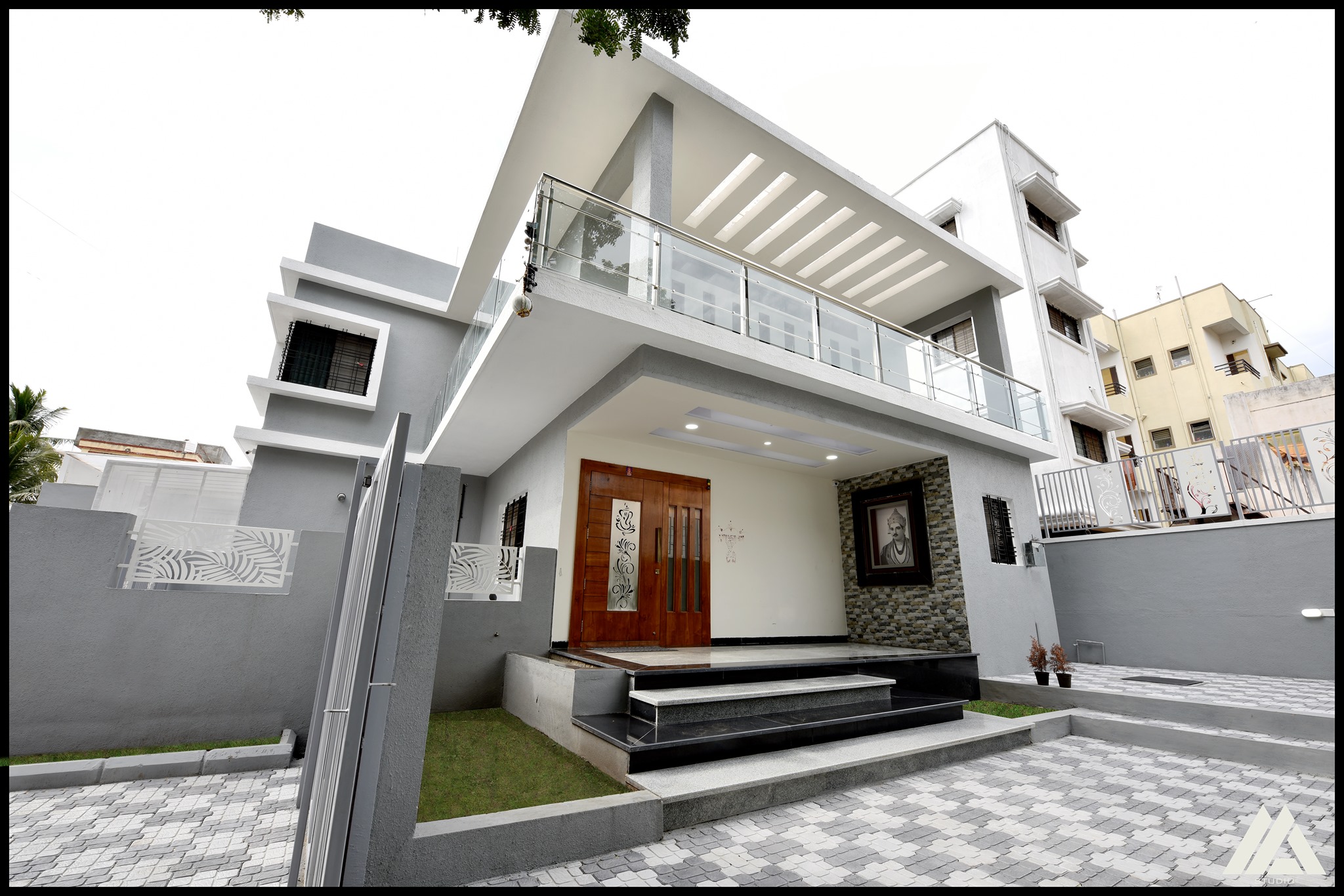 A double-storied building of white and grey modern exteriors with an entrance and extended balcony