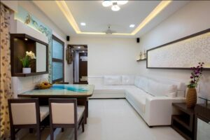 The Compact Living Room with White & Brown Combination has L Shaped White Upholstered Sofa with Wooden Side Table cum Storage Unit - 2